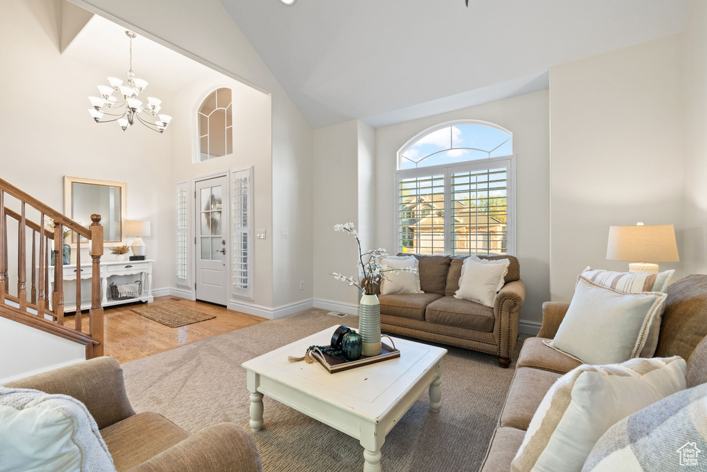 Living area featuring high vaulted ceiling, a chandelier, stairs, baseboards, and wood finished floors