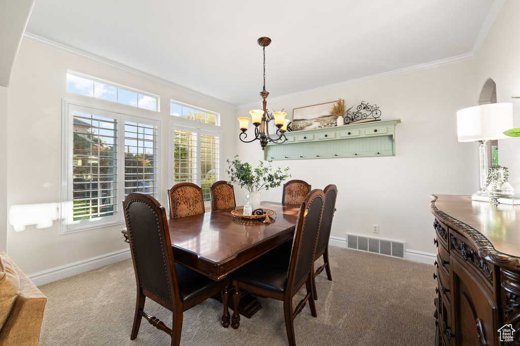 Dining room with a chandelier, light carpet, ornamental molding, and baseboards