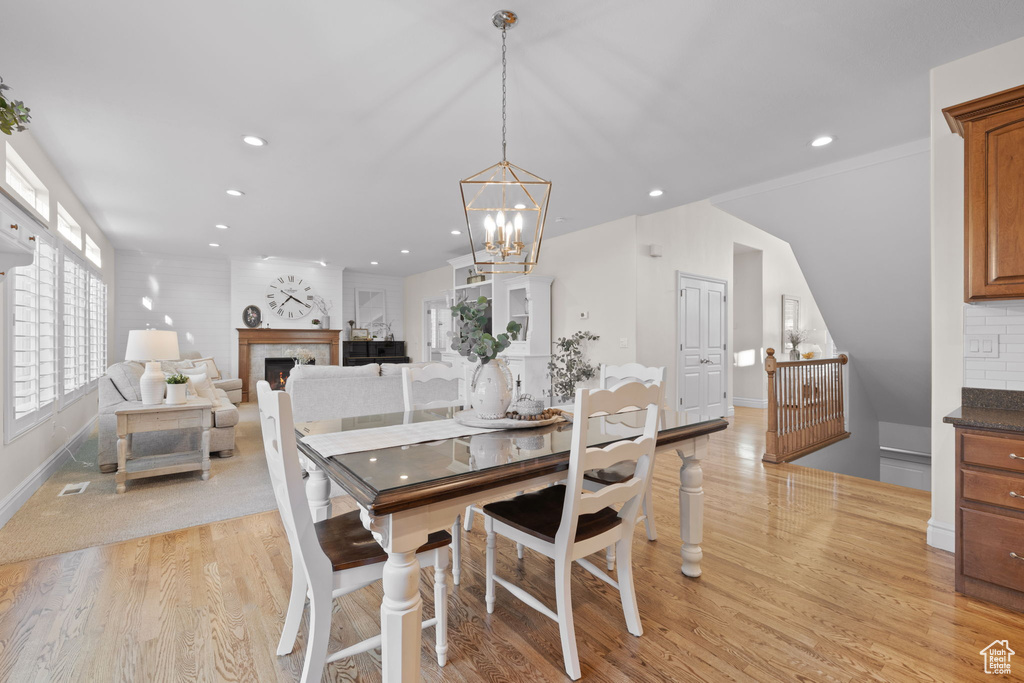 Dining room with light wood finished floors, recessed lighting, a chandelier, baseboards, and a lit fireplace