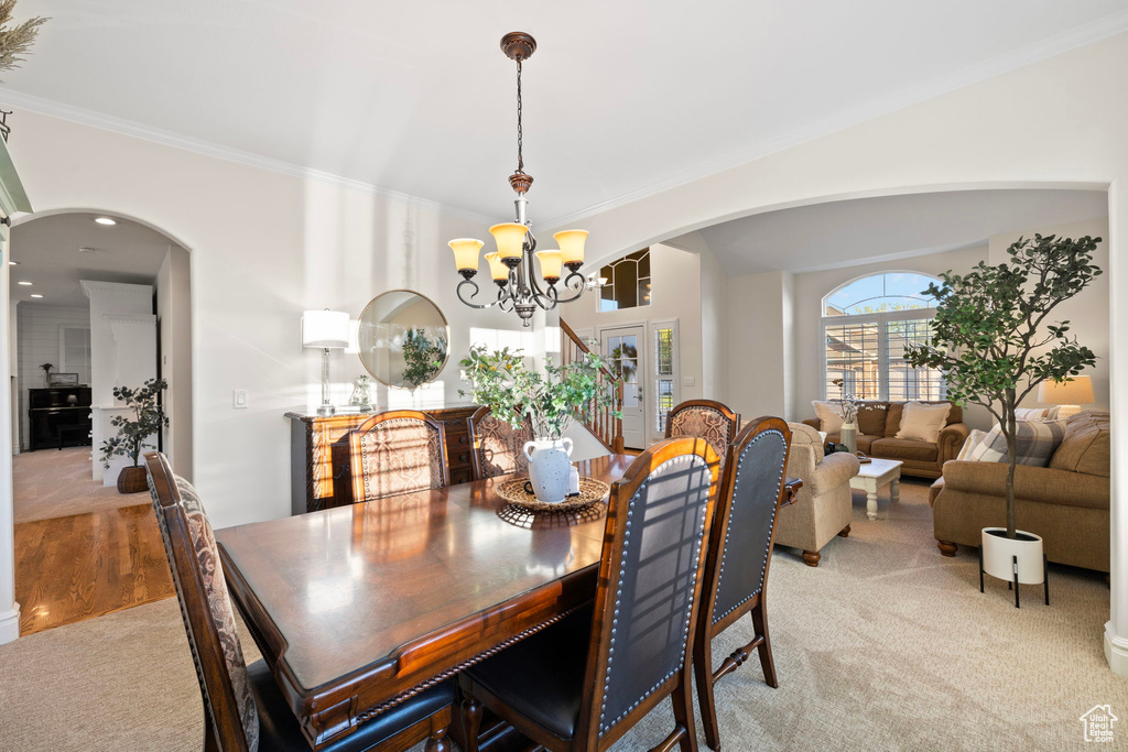Dining room featuring a chandelier, arched walkways, light colored carpet, and crown molding