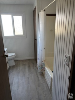 Full bath with toilet, wood finished floors, shower / bath combination with curtain, and baseboards