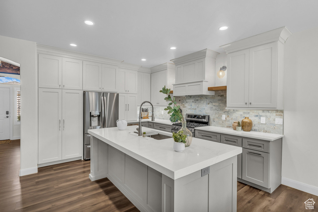 Kitchen featuring appliances with stainless steel finishes, a sink, tasteful backsplash, light countertops, and dark wood finished floors
