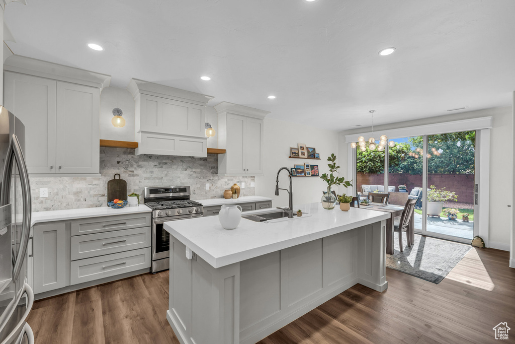 Kitchen featuring appliances with stainless steel finishes, a sink, light countertops, backsplash, and a center island with sink