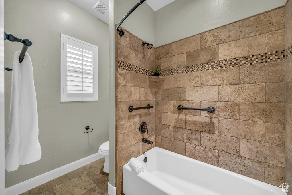 Full bath featuring shower / bathtub combination, toilet, baseboards, and stone finish floors