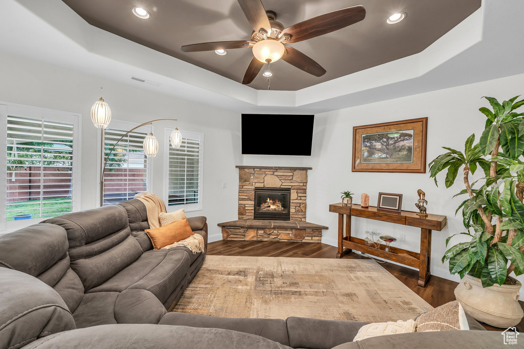 Living room with a tray ceiling, baseboards, ceiling fan, wood finished floors, and a stone fireplace