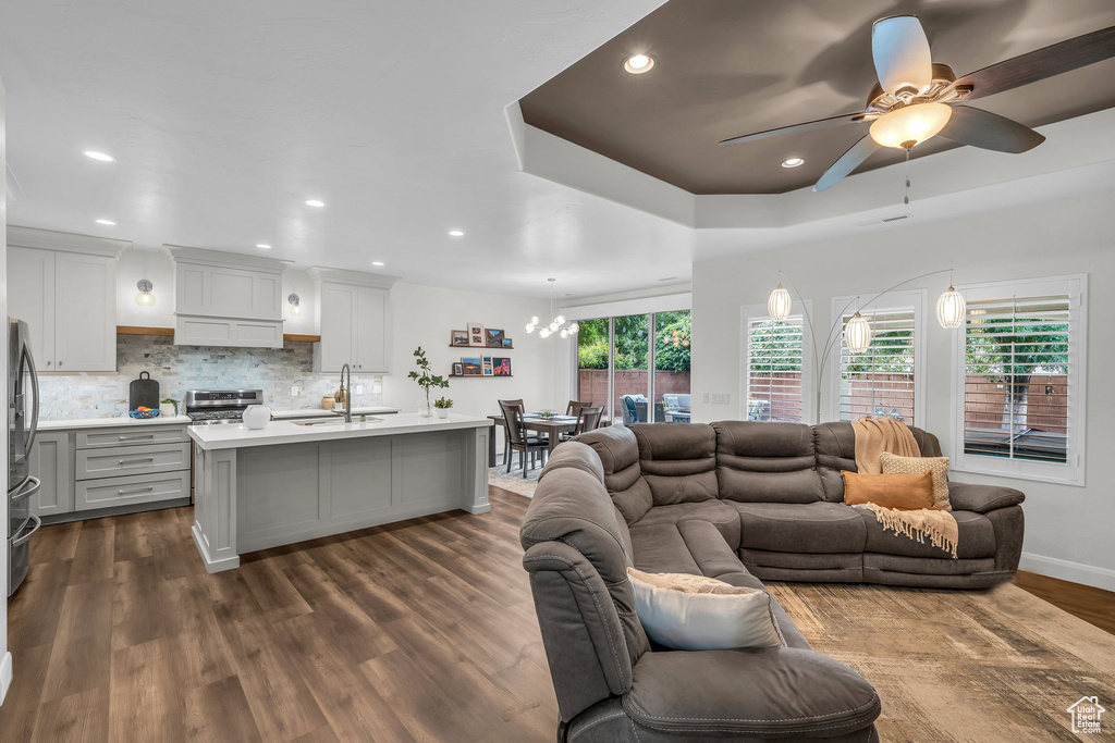 Living area featuring a ceiling fan, dark wood-style floors, recessed lighting, baseboards, and a chandelier