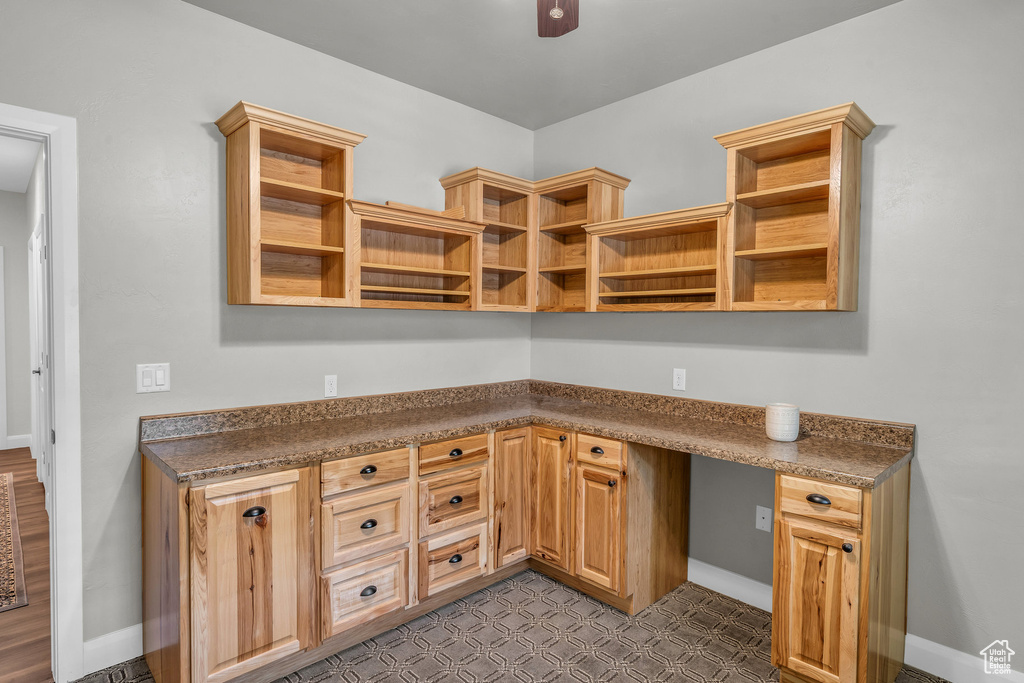 Unfurnished office featuring built in desk, dark floors, ceiling fan, and baseboards