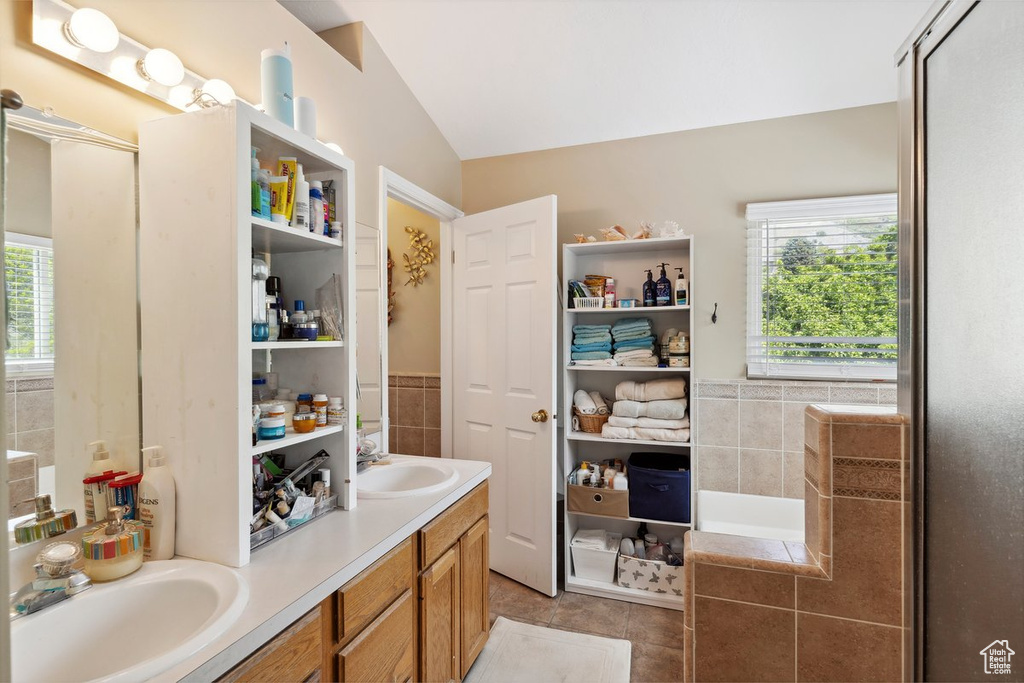 Full bathroom with healthy amount of natural light, lofted ceiling, tile patterned flooring, tile walls, and double vanity