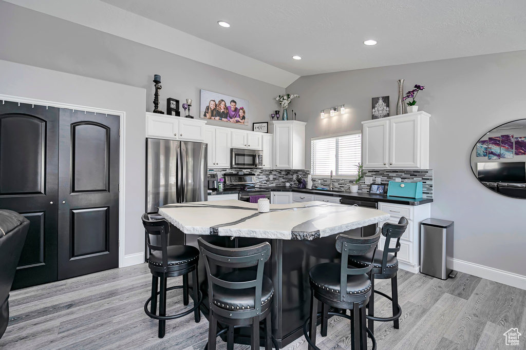 Kitchen with stainless steel appliances, vaulted ceiling, decorative backsplash, white cabinets, and a breakfast bar area