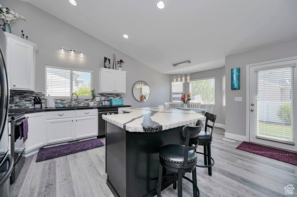 Kitchen featuring a sink, lofted ceiling, dishwashing machine, a kitchen bar, and backsplash