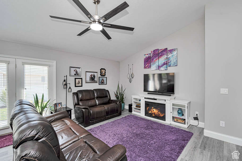 Living room with wood finished floors, a ceiling fan, a lit fireplace, vaulted ceiling, and baseboards