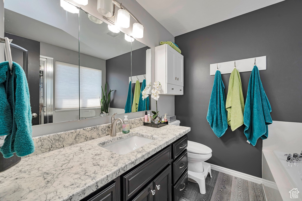 Bathroom with wood finished floors, baseboards, vanity, toilet, and a bath