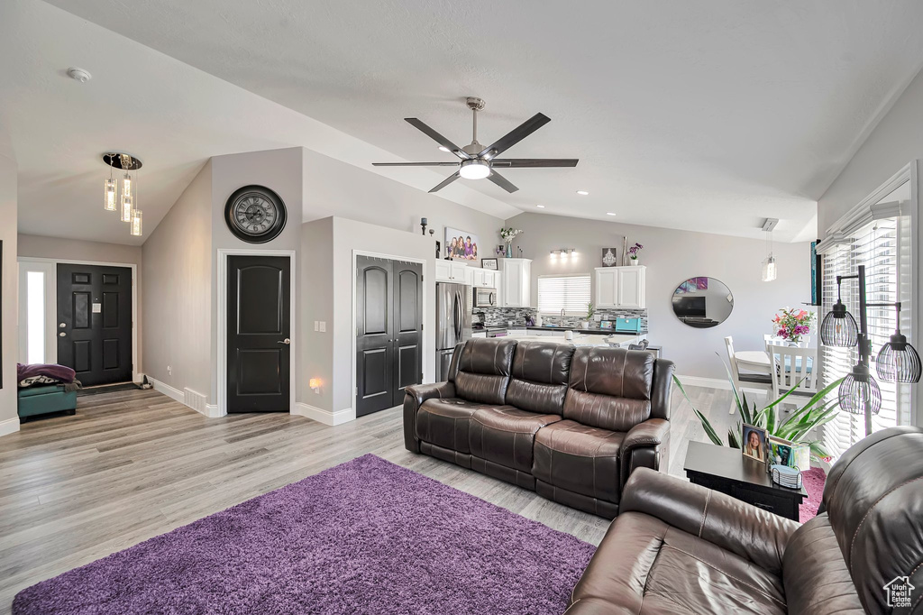 Living room with lofted ceiling, ceiling fan, light wood-type flooring, and baseboards