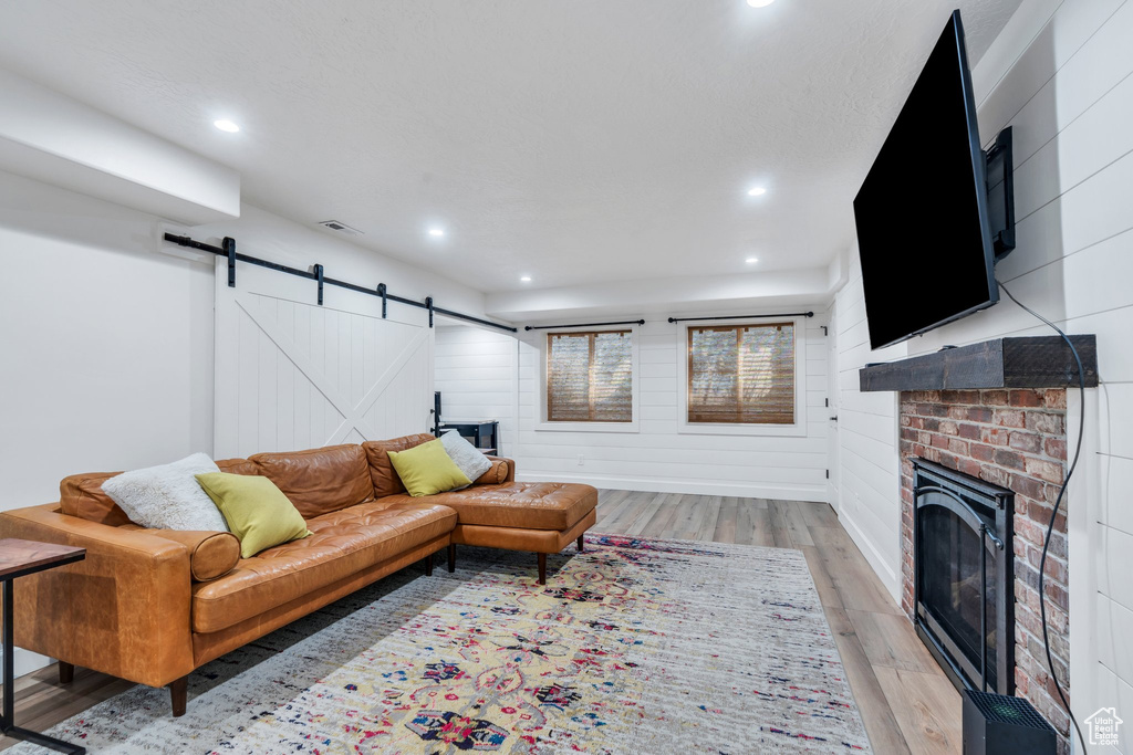 Living area with a barn door, light wood-type flooring, a fireplace, and recessed lighting