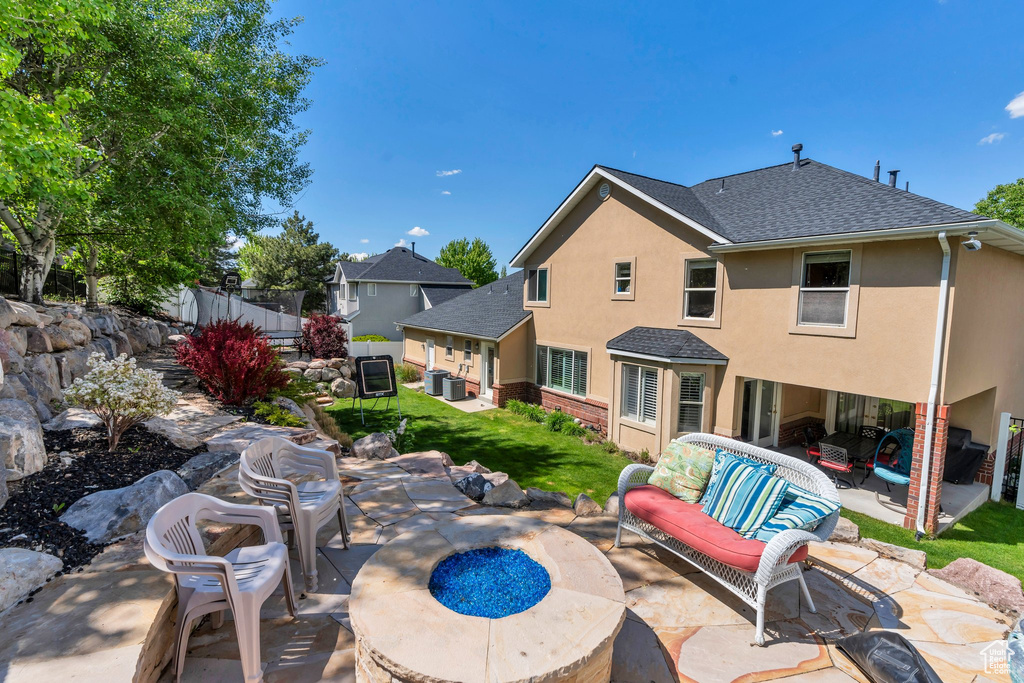 Back of house featuring an outdoor living space with a fire pit, a patio, stucco siding, roof with shingles, and central AC unit