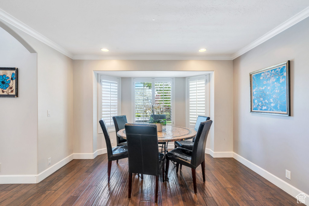 Dining area with dark wood-style floors, crown molding, baseboards, recessed lighting, and arched walkways