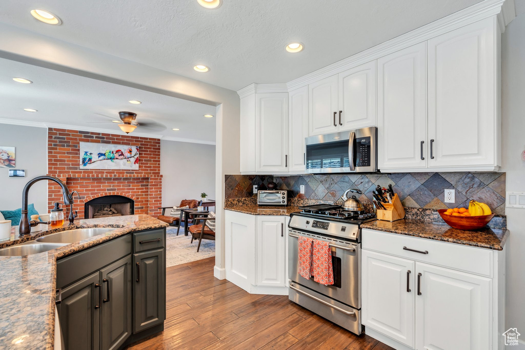 Kitchen with stainless steel appliances, a sink, a fireplace, white cabinetry, and wood finished floors