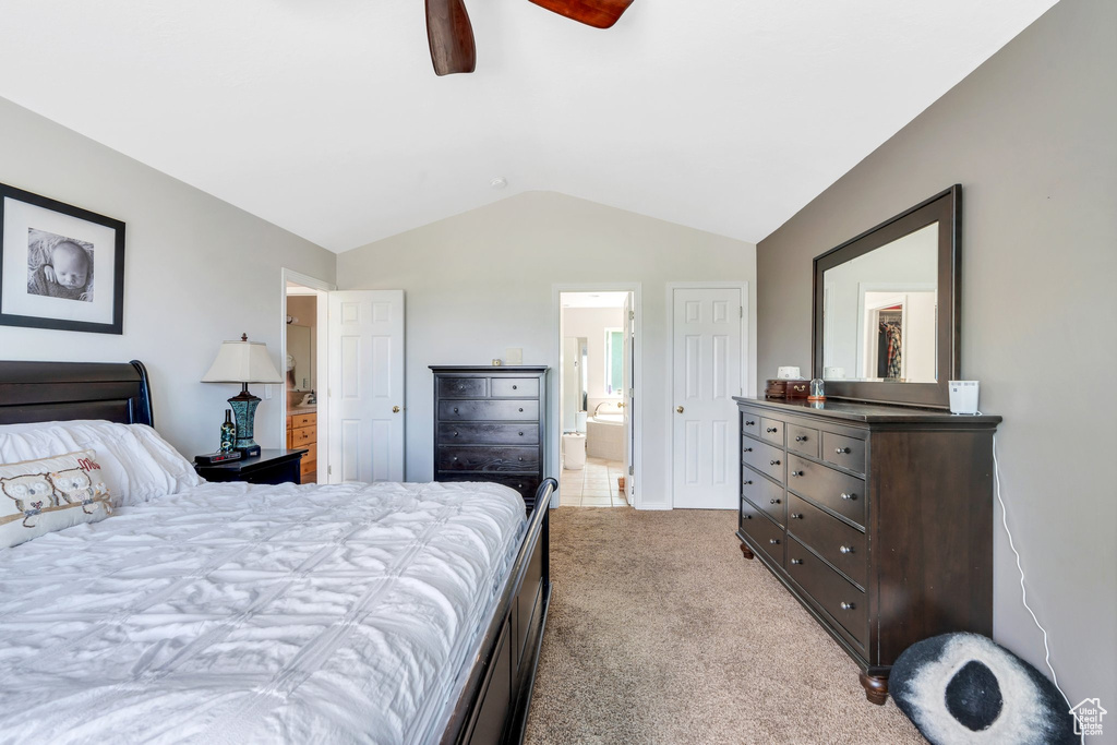 Bedroom featuring vaulted ceiling, light colored carpet, ensuite bath, and a ceiling fan
