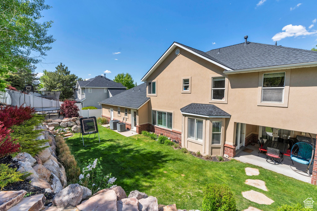 Back of house featuring a trampoline, a patio area, a shingled roof, brick siding, and stucco siding