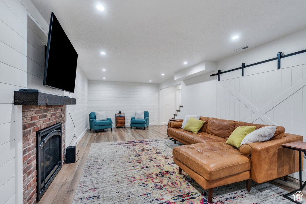 Living room with a barn door, wood finished floors, a fireplace, stairway, and recessed lighting
