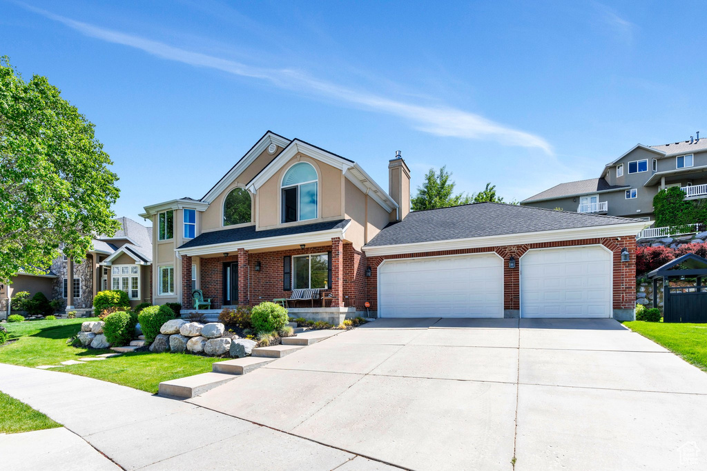 Traditional-style house with an attached garage, concrete driveway, covered porch, brick siding, and a chimney