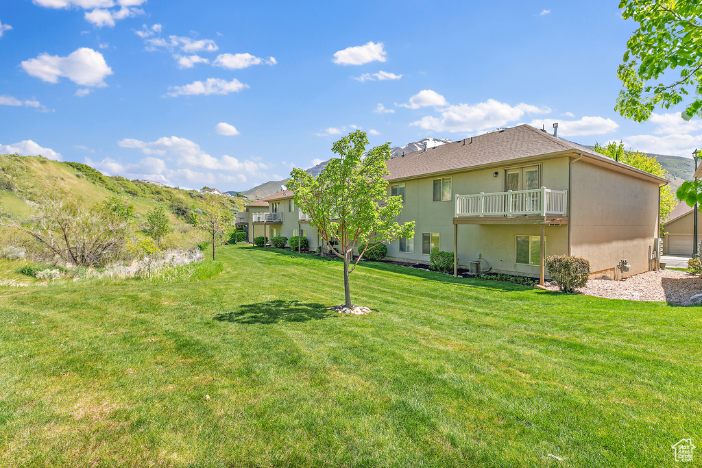 Back of house featuring a balcony, a yard, and stucco siding