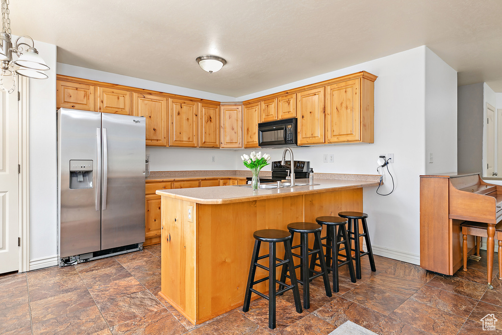 Kitchen with black appliances, stone finish flooring, a peninsula, a kitchen bar, and baseboards
