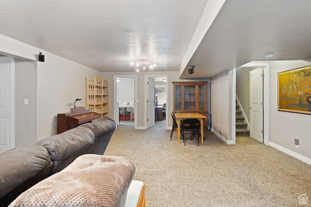 Living area featuring light carpet, stairway, baseboards, and a textured ceiling