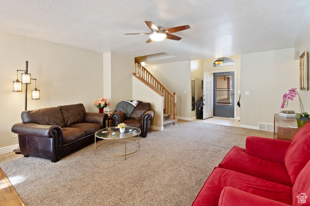 Carpeted living area featuring stairs, baseboards, ceiling fan, and a textured ceiling