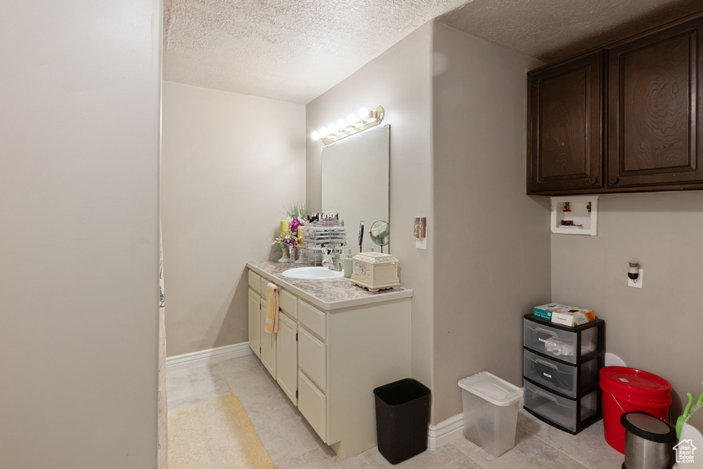 Bathroom with a textured ceiling, vanity, baseboards, and tile patterned flooring