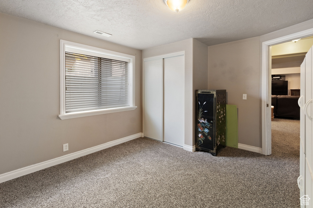 Unfurnished bedroom featuring carpet flooring, a textured ceiling, a closet, and baseboards
