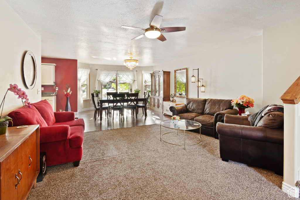 Carpeted living area with a ceiling fan, a textured ceiling, and baseboards