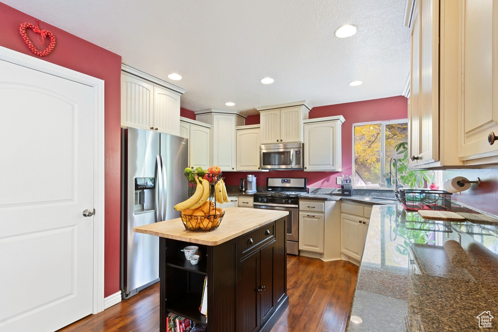 Kitchen with appliances with stainless steel finishes, a sink, butcher block countertops, dark wood-style floors, and a center island