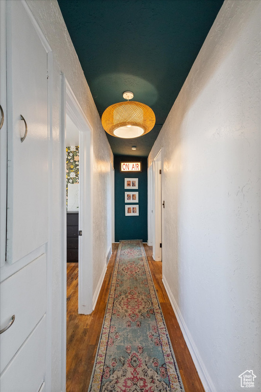 Hallway featuring a textured wall, baseboards, and wood finished floors