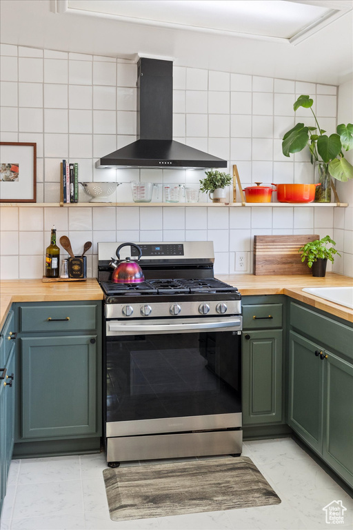 Kitchen featuring stainless steel gas range oven, green cabinets, butcher block counters, wall chimney exhaust hood, and backsplash