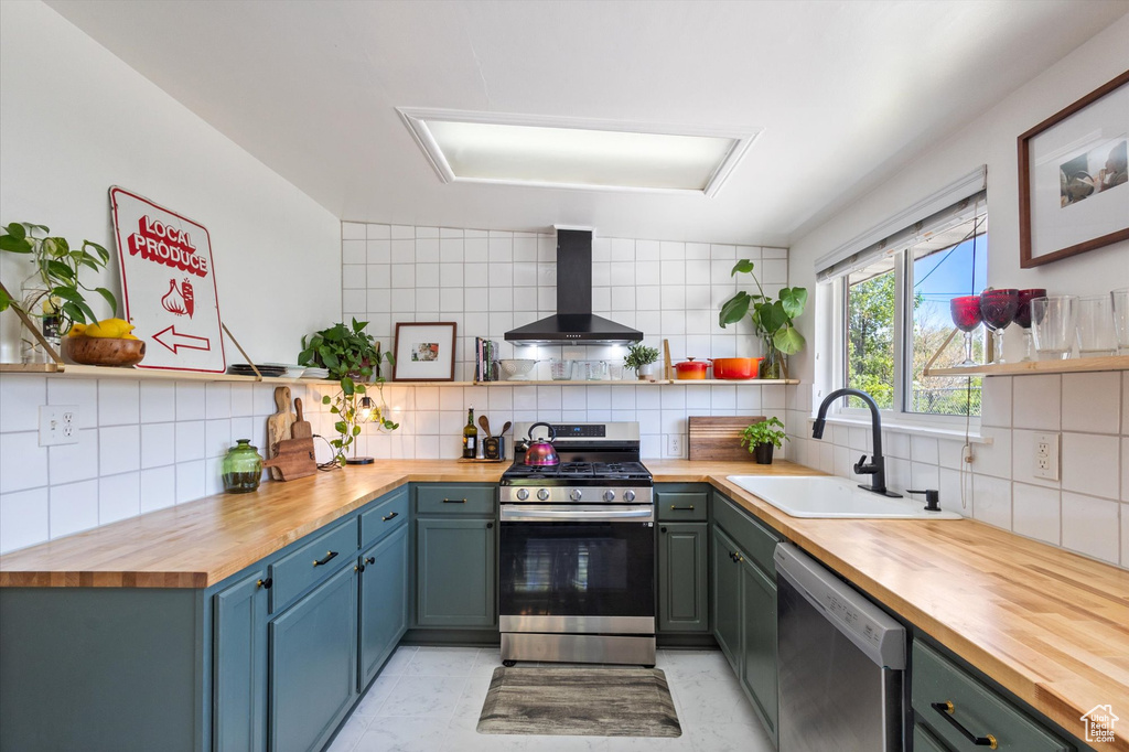 Kitchen featuring a sink, wall chimney range hood, wood counters, open shelves, and appliances with stainless steel finishes