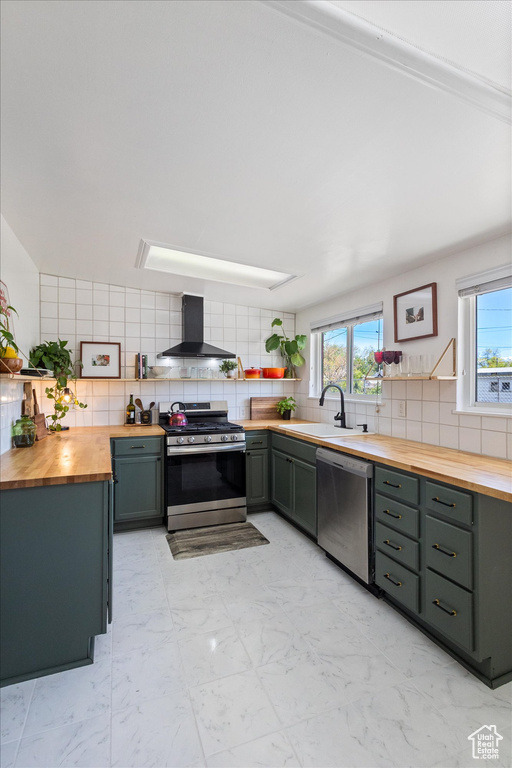 Kitchen featuring backsplash, wall chimney range hood, stainless steel appliances, and butcher block countertops