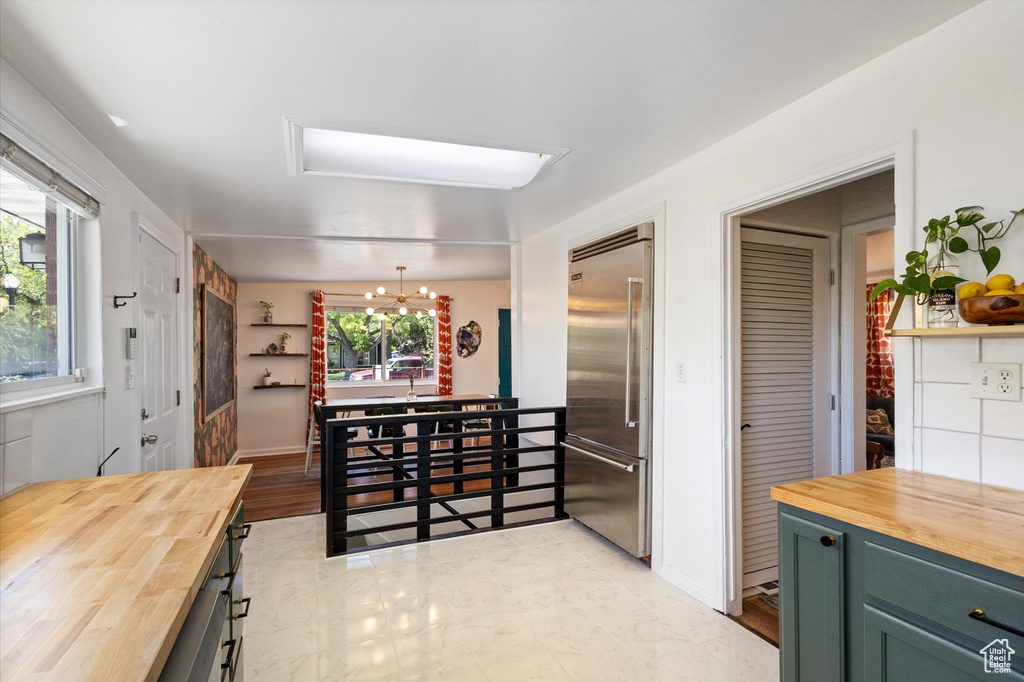 Kitchen with butcher block countertops, a chandelier, built in fridge, and green cabinetry