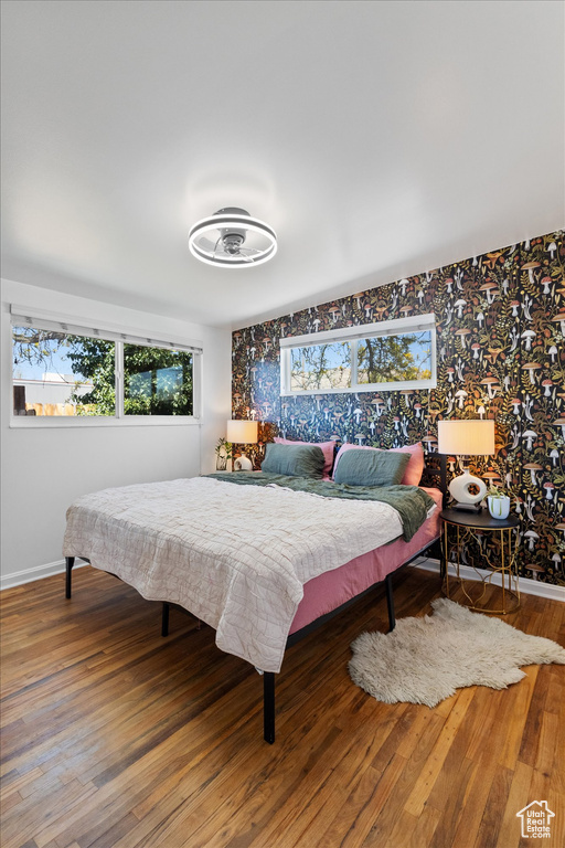 Bedroom with wallpapered walls, wood finished floors, and baseboards