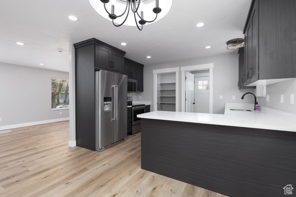 Kitchen with stainless steel appliances, a sink, a peninsula, light wood finished floors, and light countertops