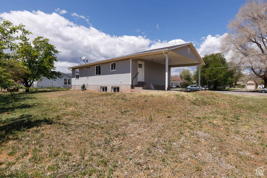 Rear view of property with an attached carport, a lawn, and entry steps