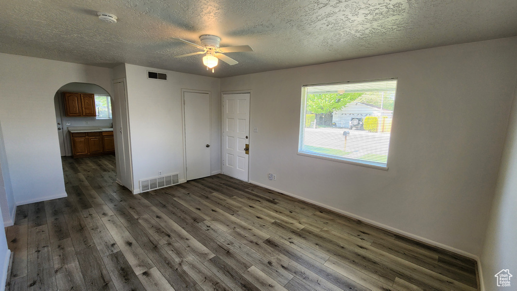 Unfurnished room featuring arched walkways, ceiling fan, dark wood-style floors, a smoke detector, and a textured ceiling