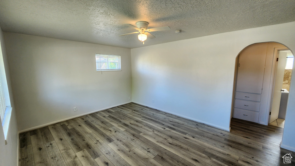 Unfurnished room featuring arched walkways, ceiling fan, wood finished floors, a textured ceiling, and baseboards