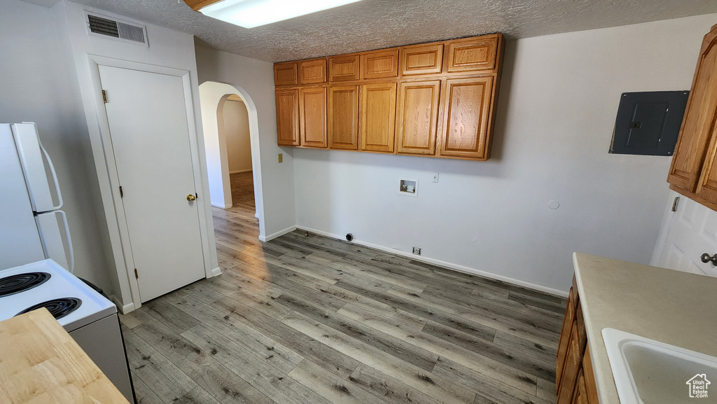 Washroom with electric panel, hookup for a gas dryer, arched walkways, hookup for a washing machine, and light wood finished floors