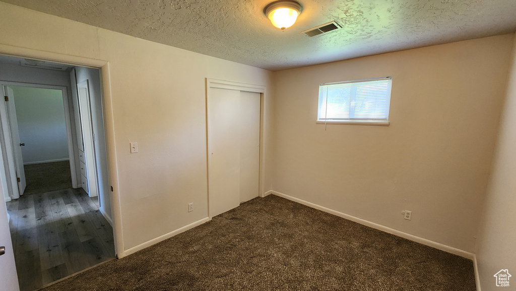 Unfurnished bedroom with a textured ceiling, a closet, baseboards, and dark colored carpet