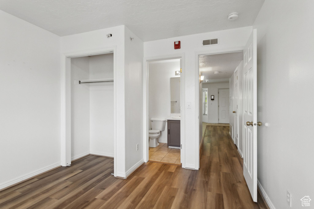 Unfurnished bedroom with wood finished floors, a closet, baseboards, and ensuite bath