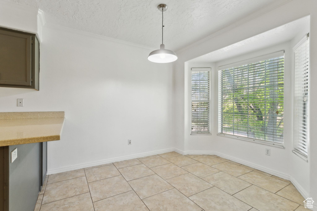 Unfurnished dining area with ornamental molding, light tile patterned floors, a textured ceiling, and baseboards
