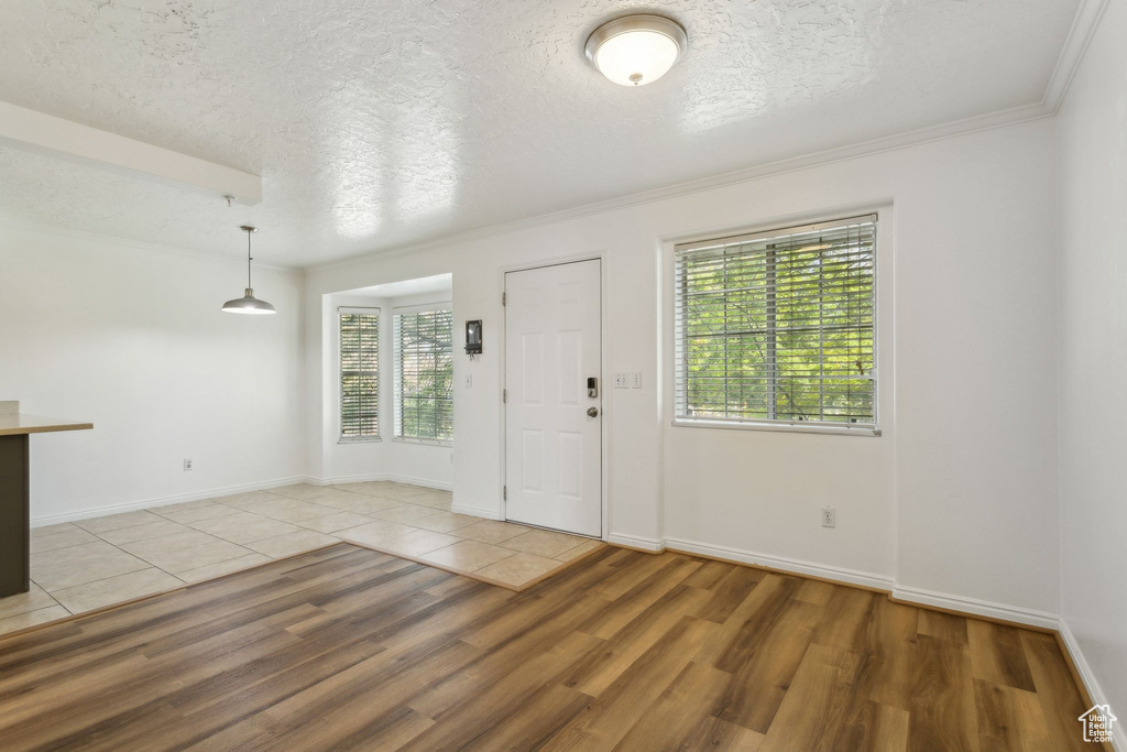 Entrance foyer with light wood-type flooring, a textured ceiling, ornamental molding, and baseboards
