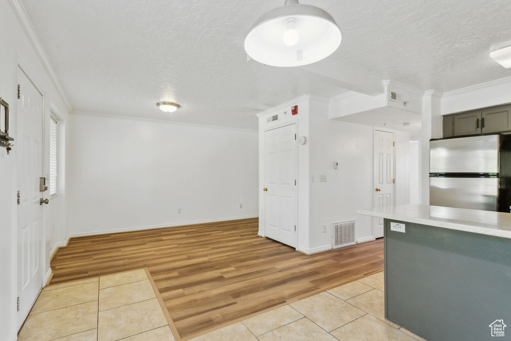 Kitchen with freestanding refrigerator, light tile patterned floors, a textured ceiling, light countertops, and crown molding