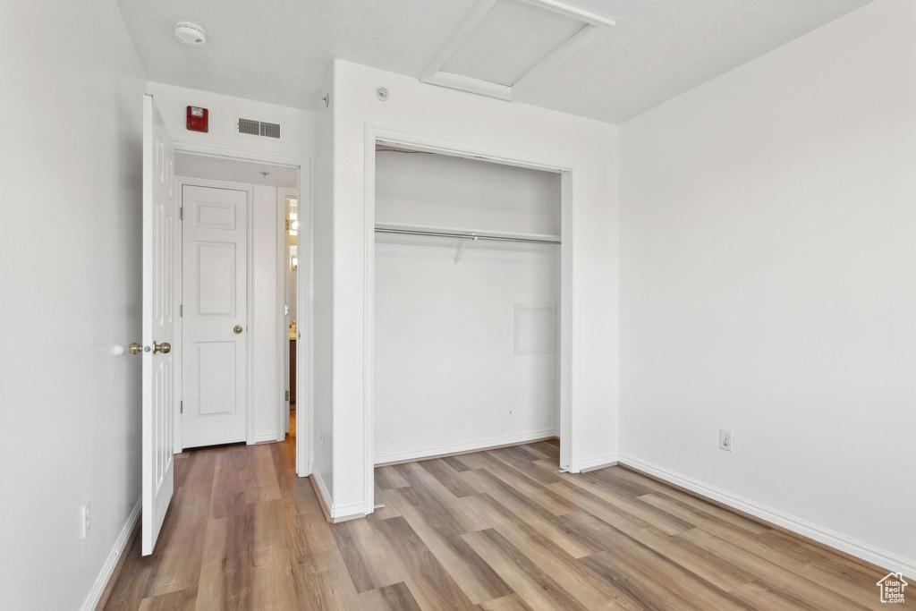 Unfurnished bedroom with attic access, wood finished floors, a closet, and baseboards